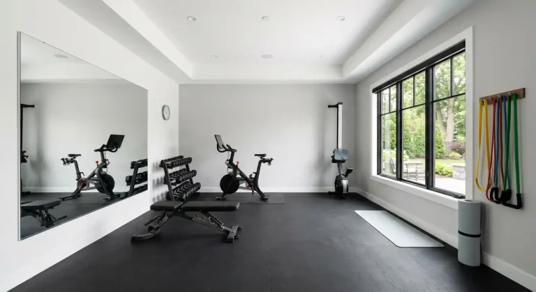 Modern home gym with exercise bike, dumbbells, workout bench, yoga mat, resistance bands, and large windows